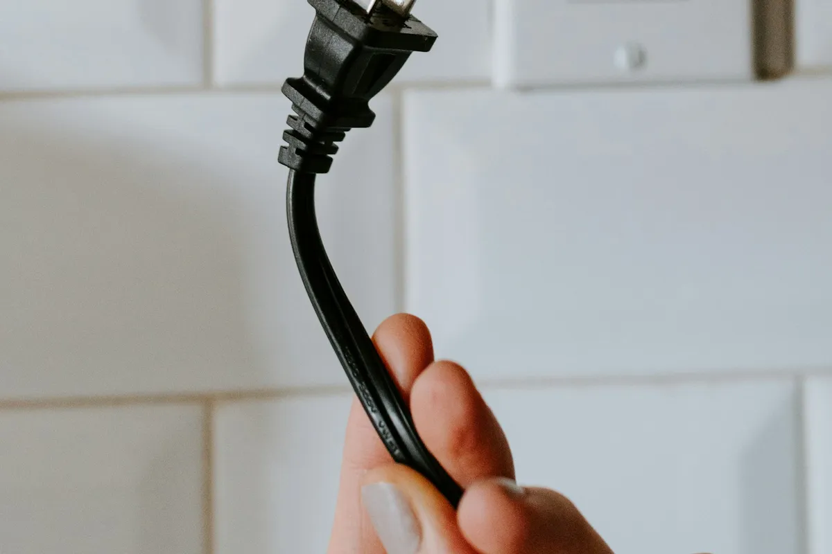 A black plug held next to a white wall outlet