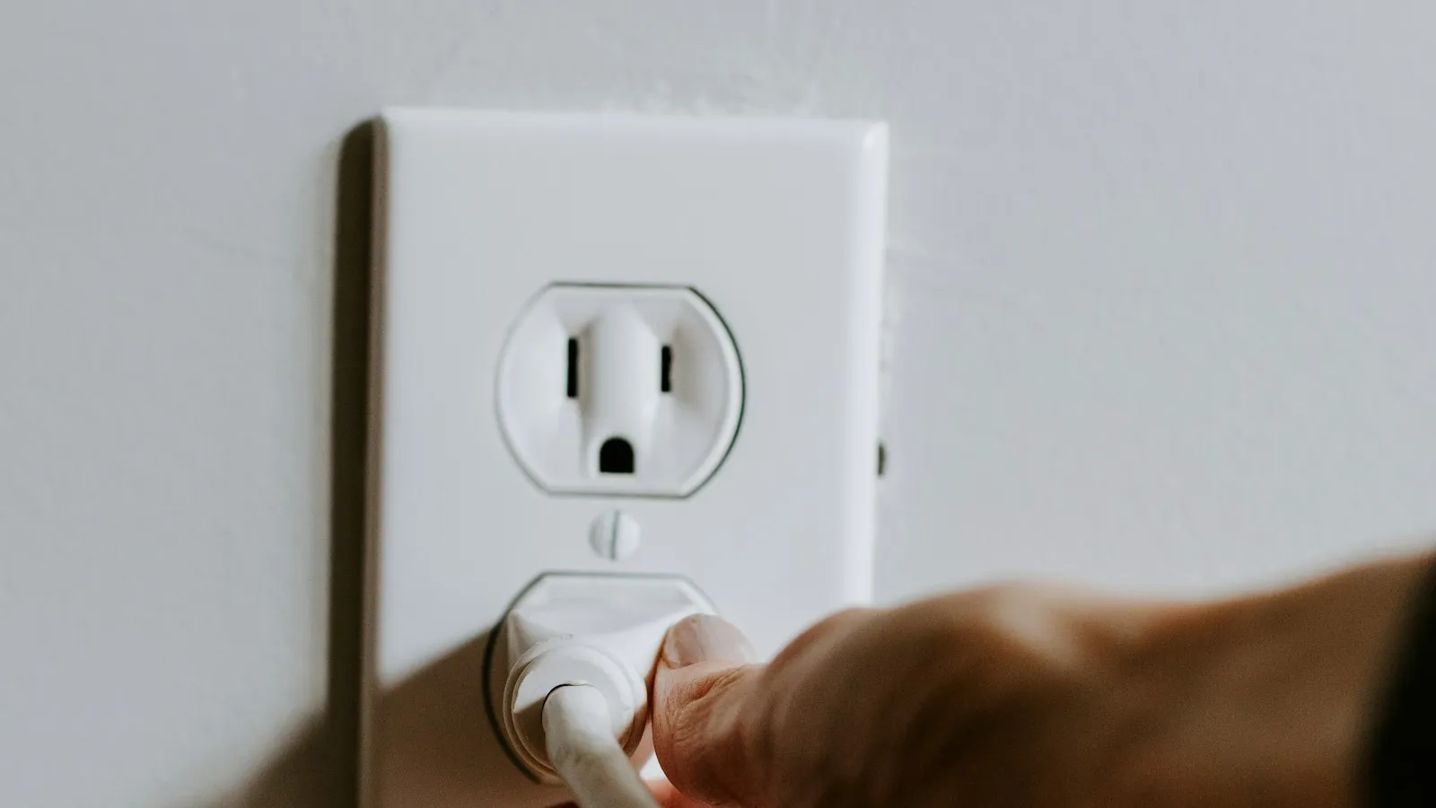 A hand plugging a white cord into a wall outlet