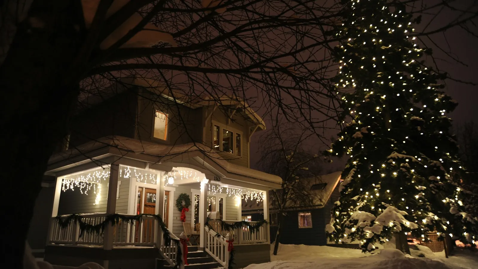A snowy porch with string lights and a lit Christmas tree