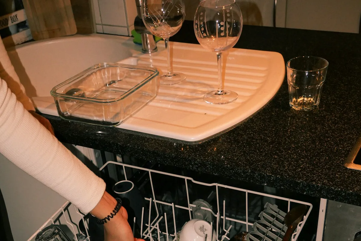 A person loading glasses into a dishwasher rack