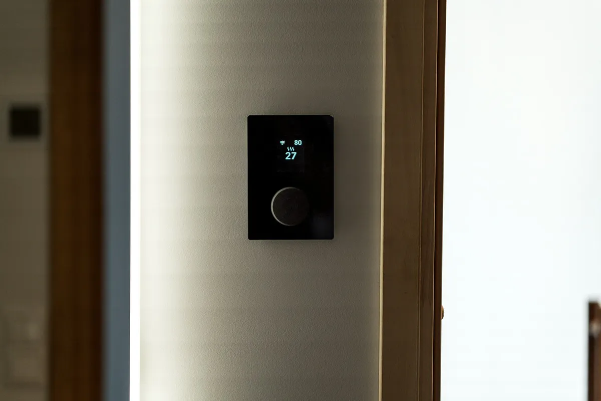 A black digital thermostat mounted on a wall