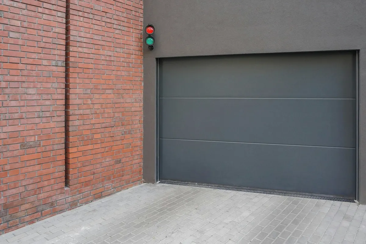 A closed gray garage door beside a brick wall