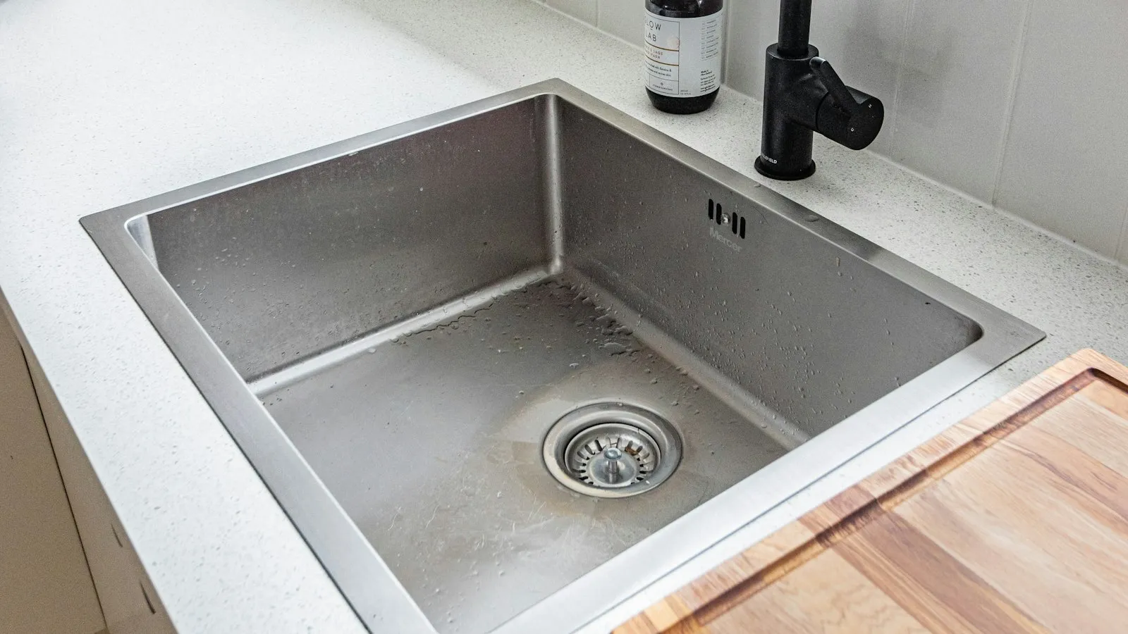 A stainless steel kitchen sink with a drain and a black faucet