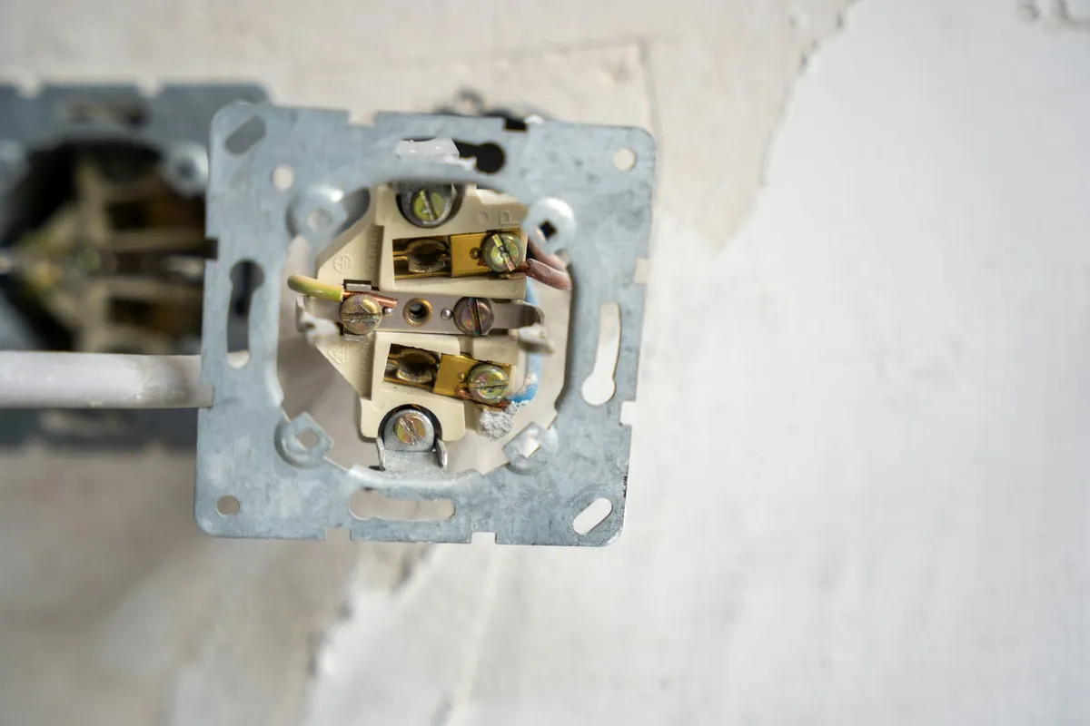 An electrical outlet removed from the wall showing the wiring