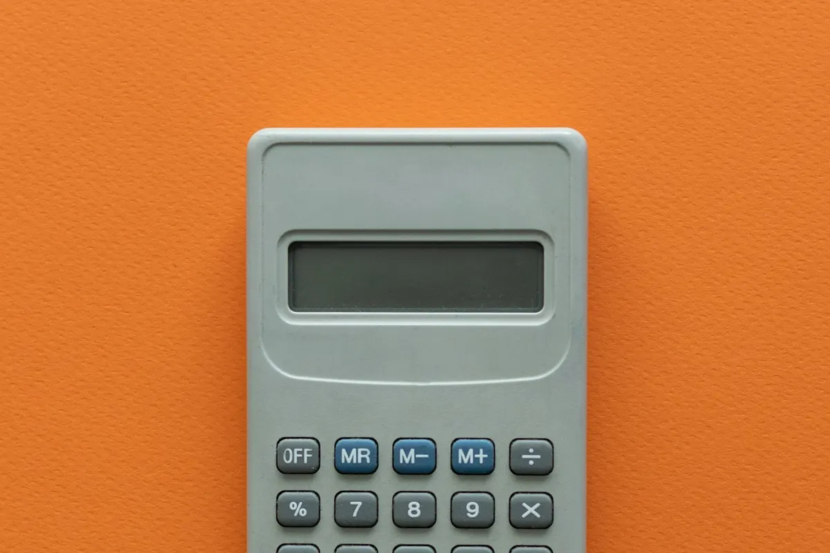 A small gray calculator lying flat on an orange background