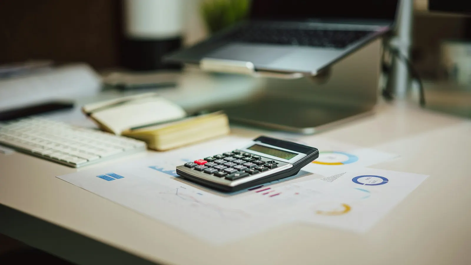 A calculator and printed charts on a desk next to a laptop