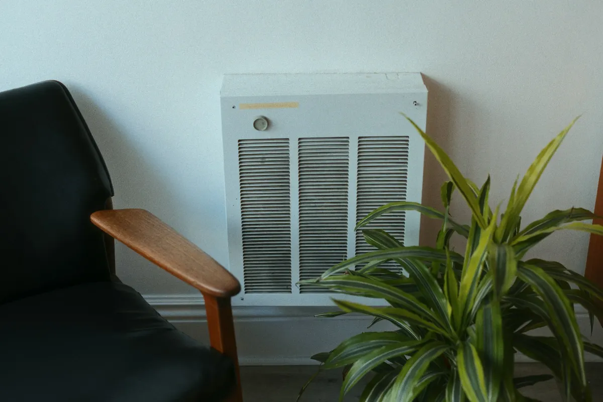 A white wall-mounted electric heater beside a plant and an armchair