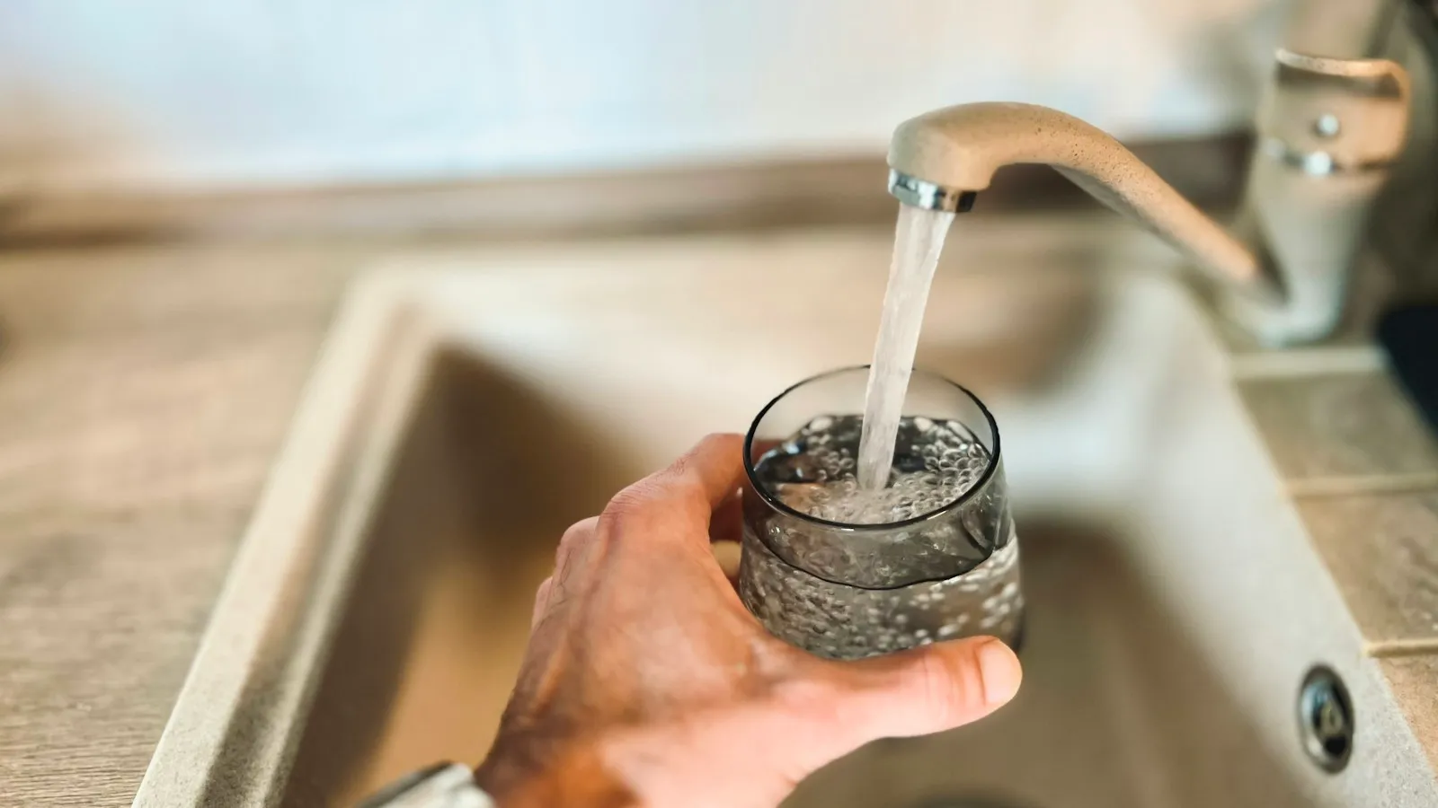 Hand filling a glass with water from a kitchen faucet