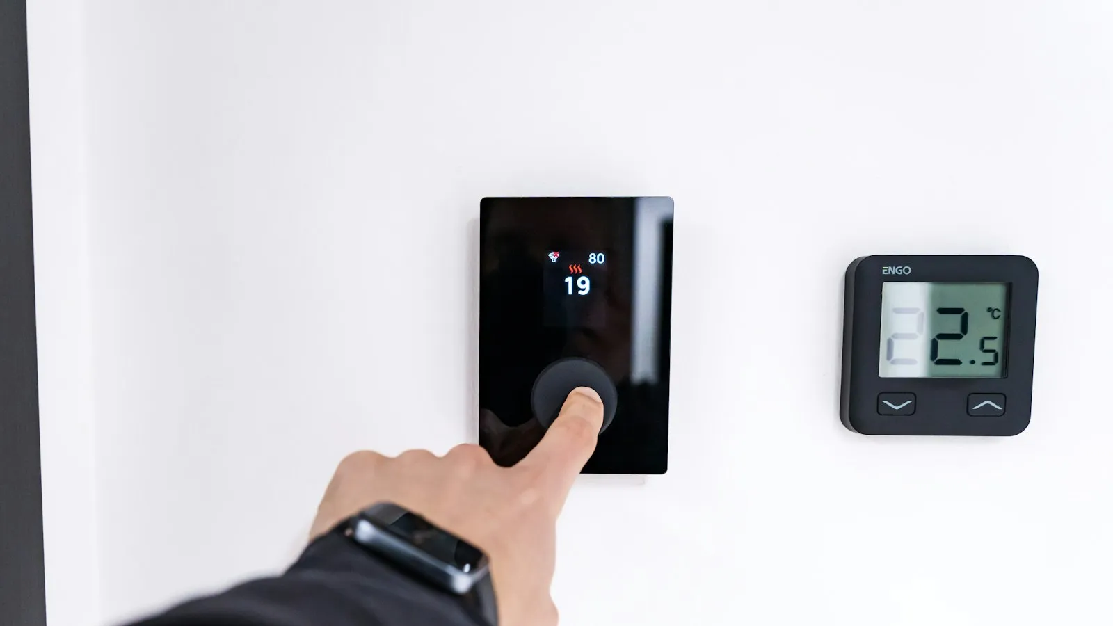 Finger turning a digital thermostat dial on a wall