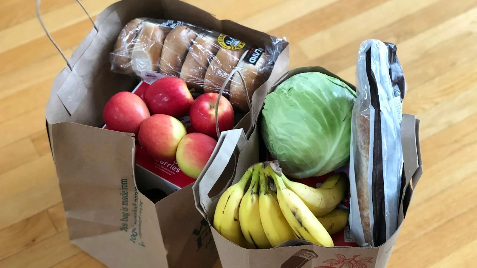 Paper grocery bags filled with apples, bananas, cabbage, and bread