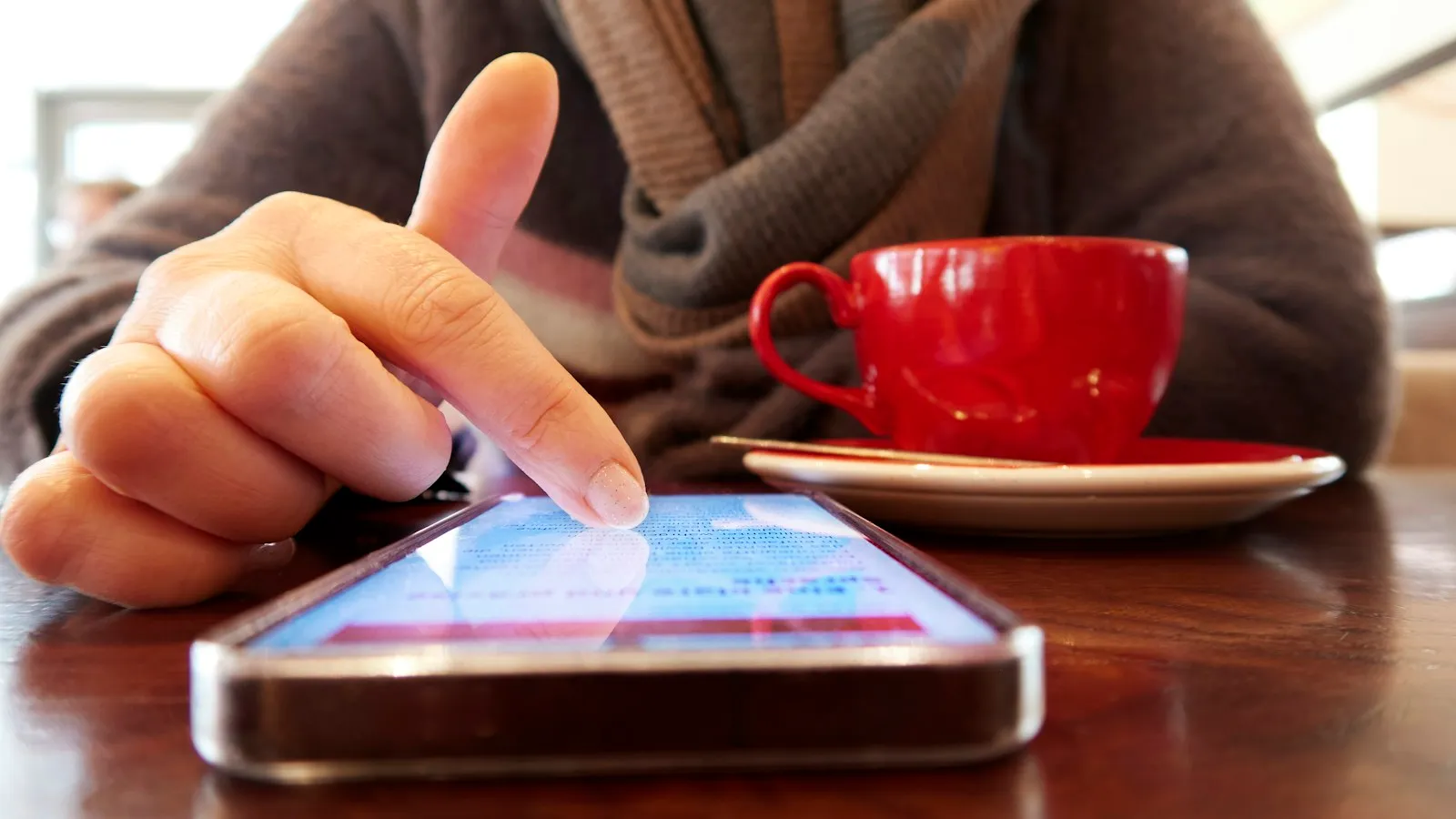 Person scrolling on a smartphone next to a red coffee cup