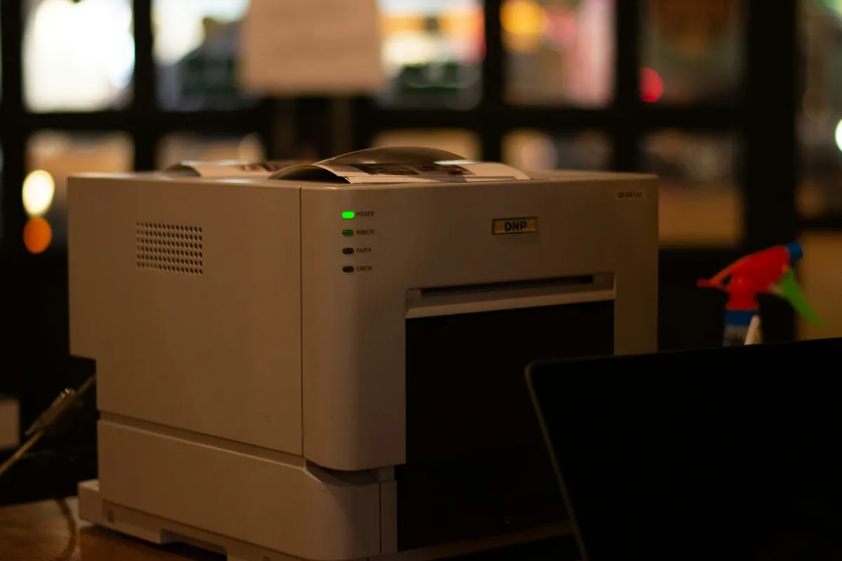 A small printer with green and dark status lights on a dim shelf