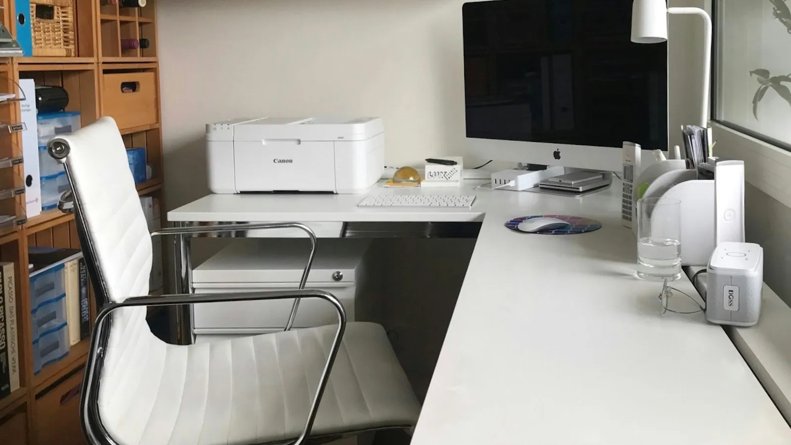 A white home printer on a desk beside a computer and a lamp