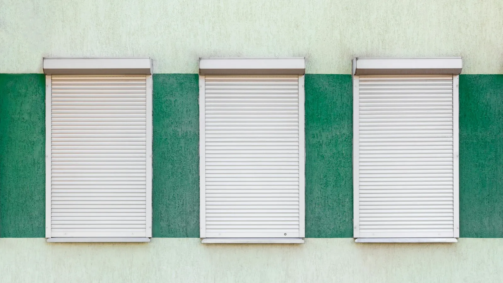 Three closed white roll-down shutters on a house wall
