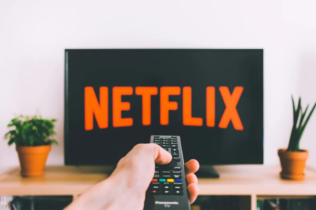A hand pointing a remote at a television with a streaming logo on the screen