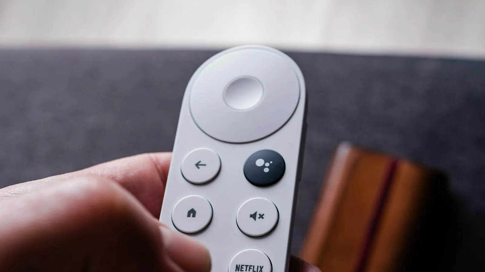 A hand holding a white streaming remote with a home button