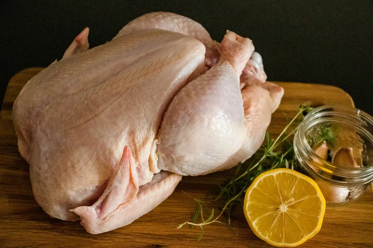 Raw whole bird on a cutting board with lemon and herbs