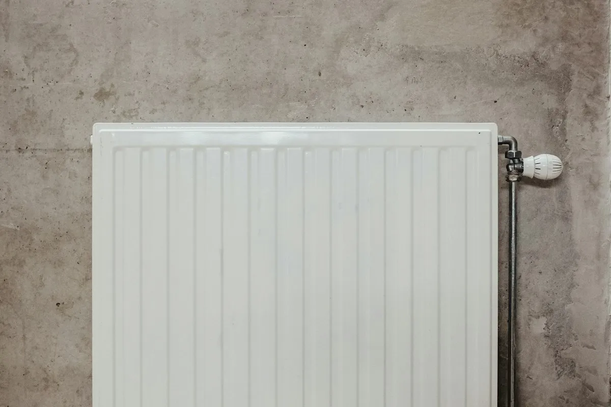 A white panel radiator on a concrete wall with a thermostatic valve