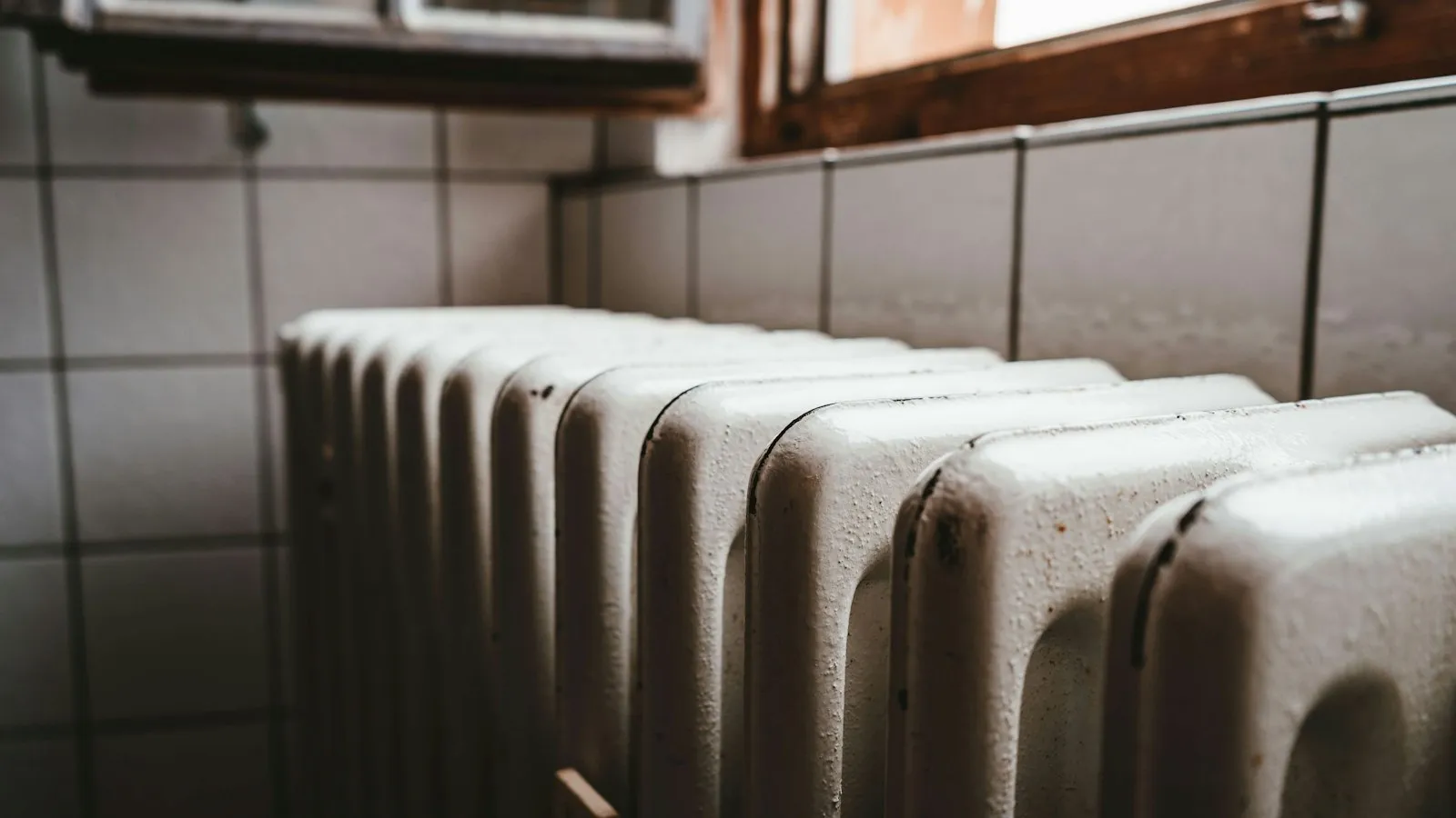 An old cast-iron radiator below a window in a tiled room