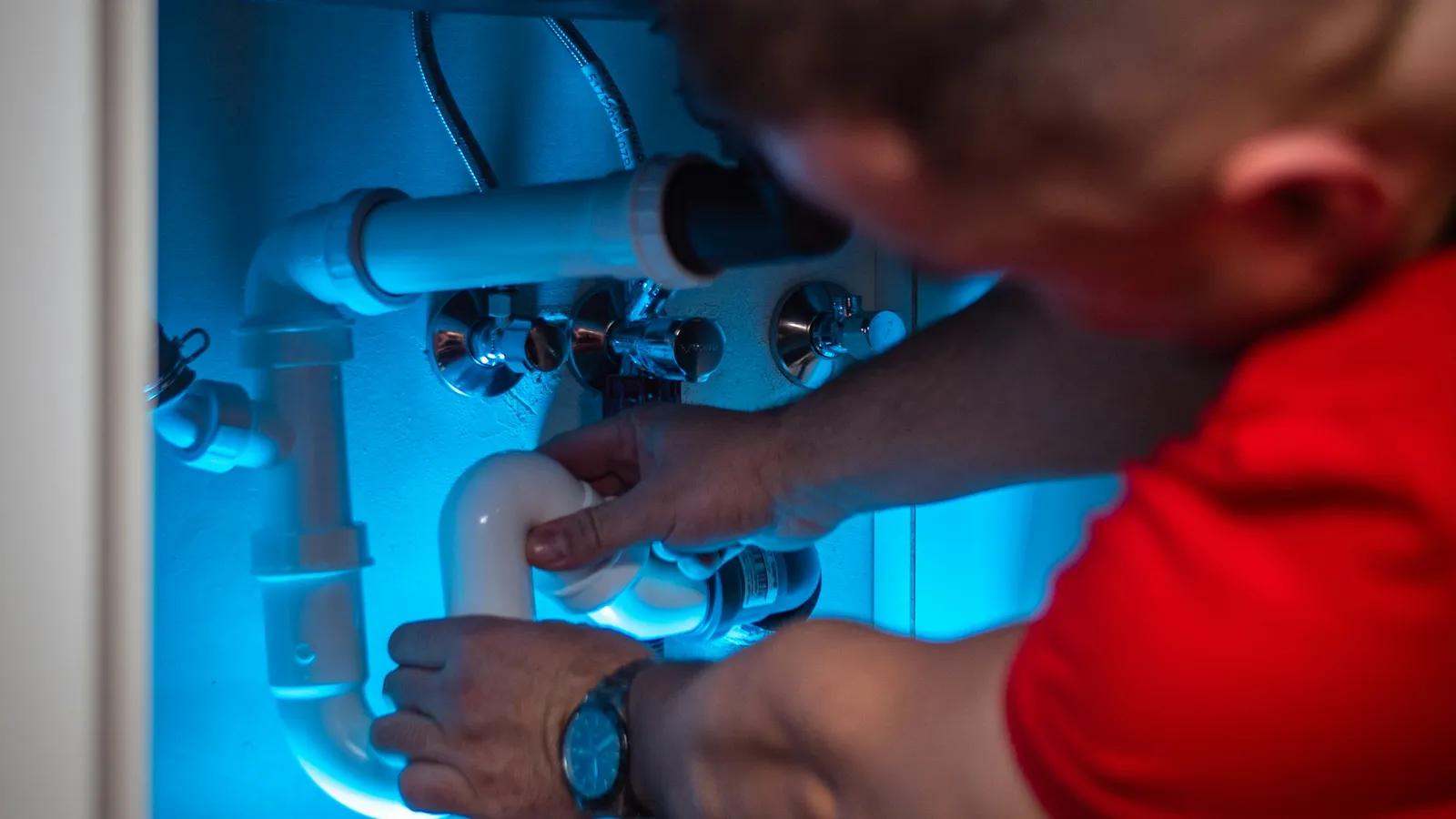 Man working on a pipe inside a cabinet