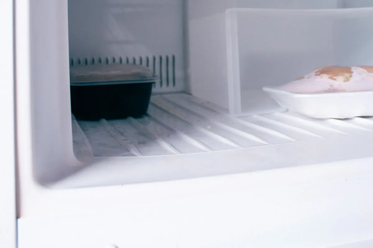 An open refrigerator with white shelves and a plate on the middle shelf