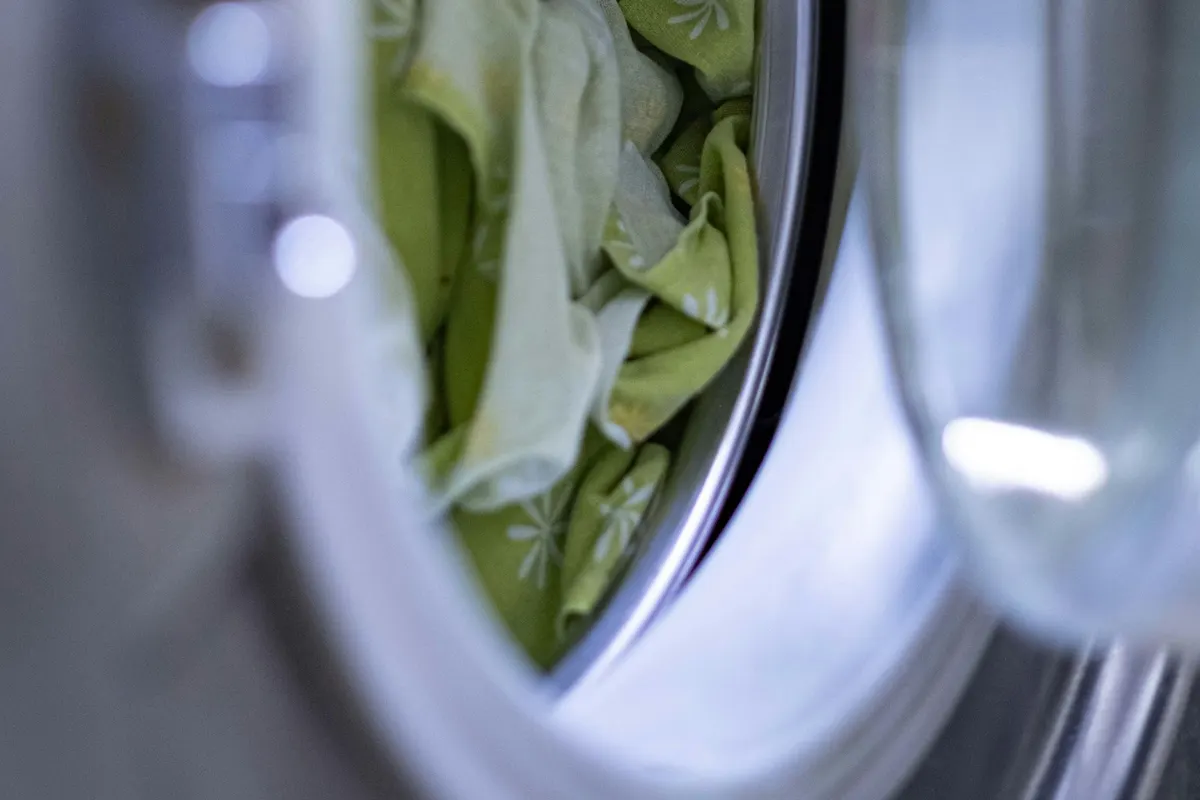 The inside of a washing machine drum with green fabric pressed against the glass