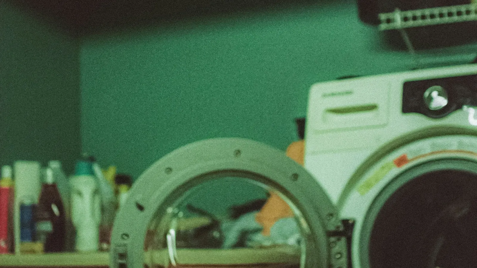A washing machine with its round door open in a green laundry room